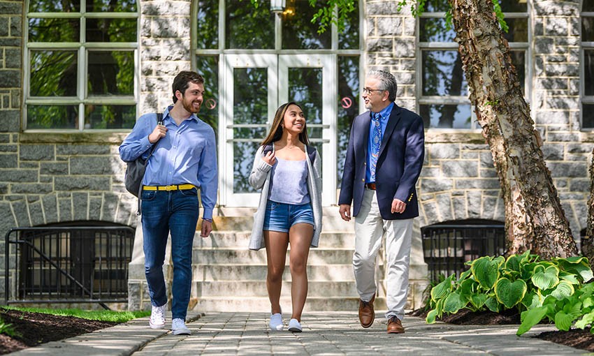 Faculty member walking with two Ӱԭ students outside Tolentine Hall.